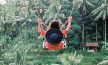 A woman swings high above the lush tropical jungle in Bali, showcasing the vibrant scenery and adventure.