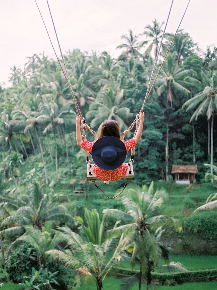 A woman swings high above the lush tropical jungle in Bali, showcasing the vibrant scenery and adventure.
