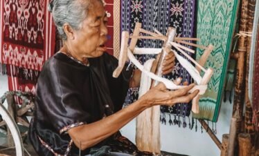 Elderly woman weaving traditional Indonesian fabrics, showcasing artisan craftsmanship.