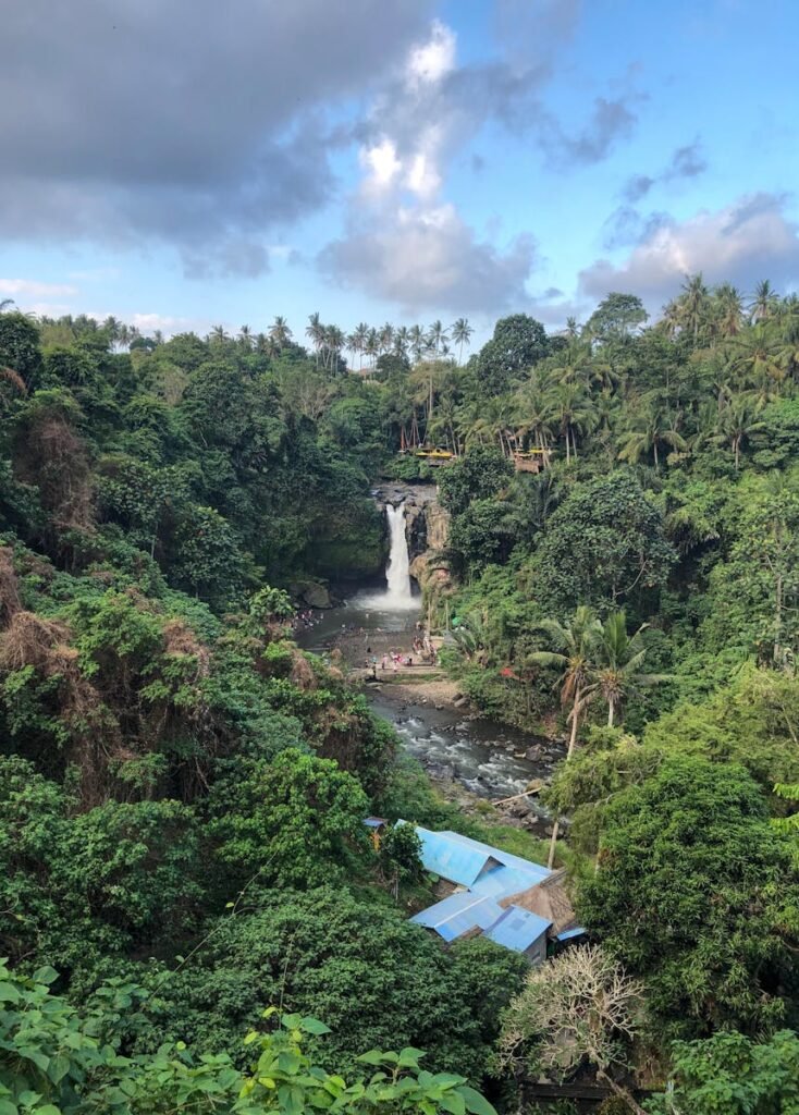 A picturesque tropical waterfall cascading amidst lush greenery and blue skies in a rural setting.